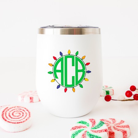White coffee mug with a green monogram on it and Christmas lights around the monogram
