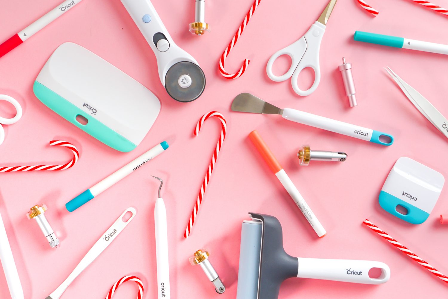 Cricut accessories and candy canes on a pink background