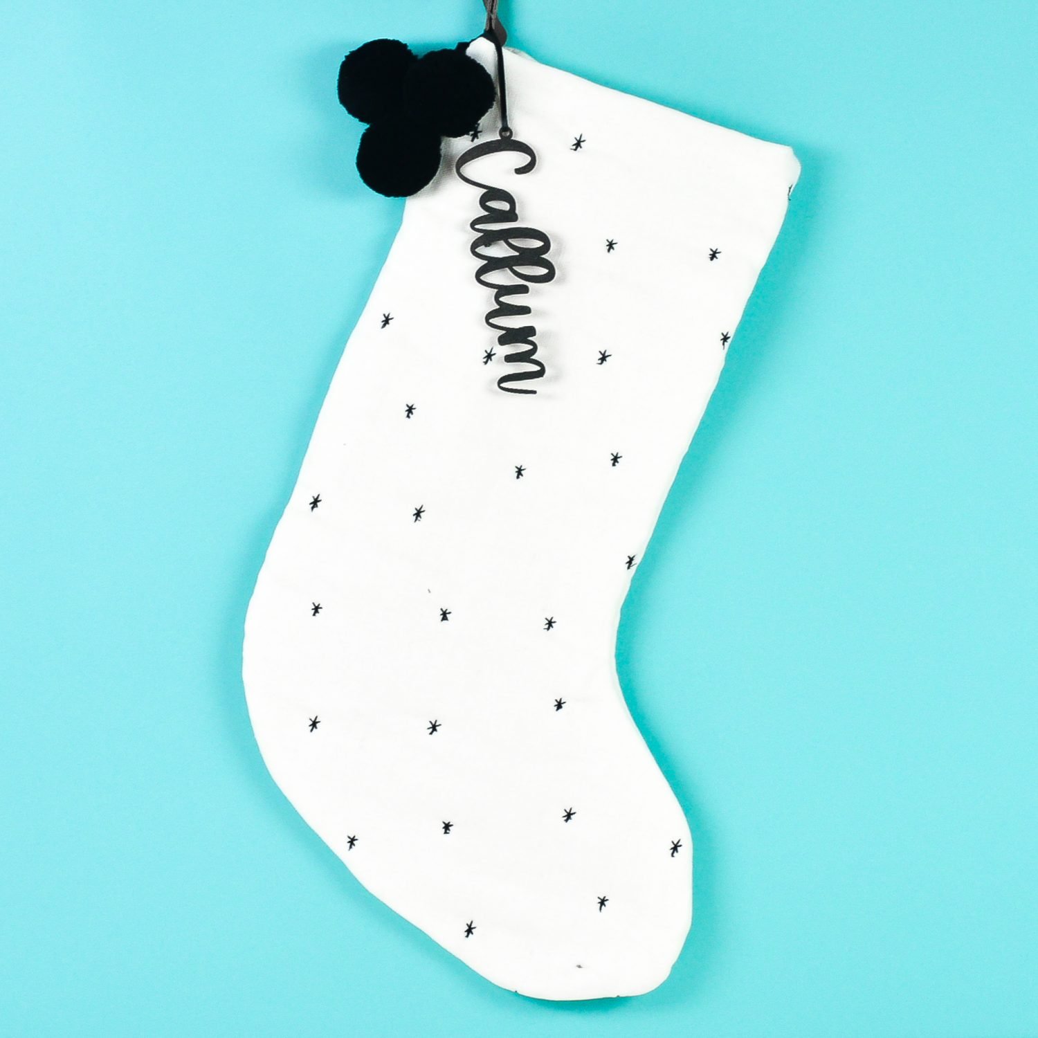 White stocking with black "Callum" personalized stocking tag on teal background