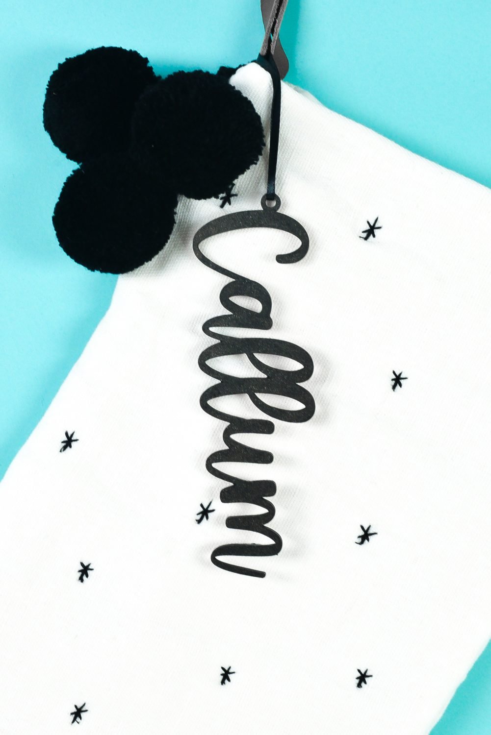 White stocking with black "Callum" personalized stocking tag on teal background