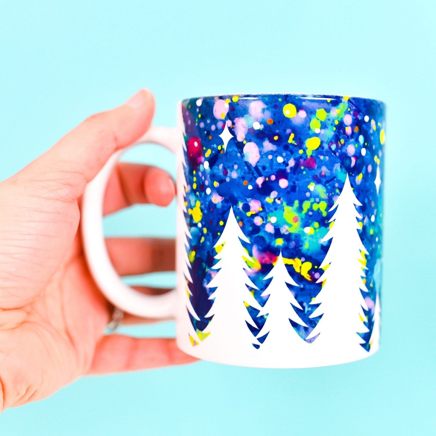 Hand holding finished mug with trees and starry sky