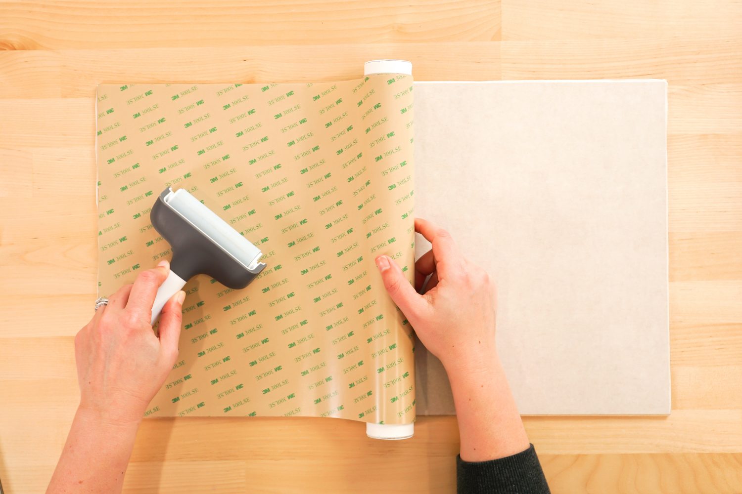 Hands using a brayer to apply the 3M adhesive