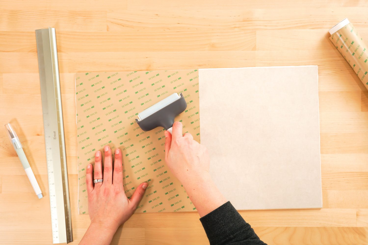 Hands using a brayer to flatten the adhesive.