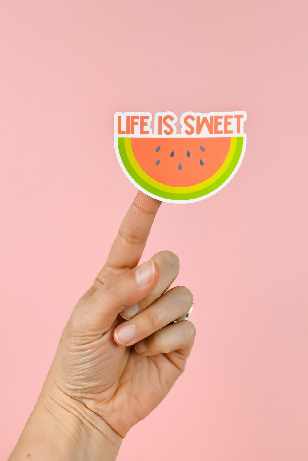 Hand holding Life is Sweet watermelon sticker over pink background