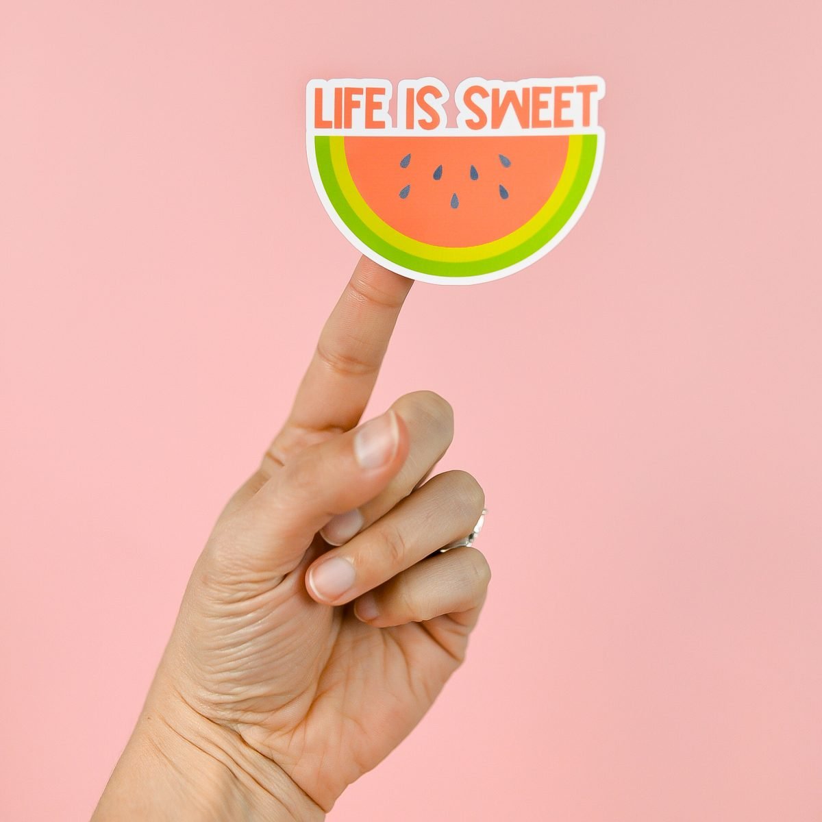 Hand holding Life is Sweet watermelon sticker over pink background