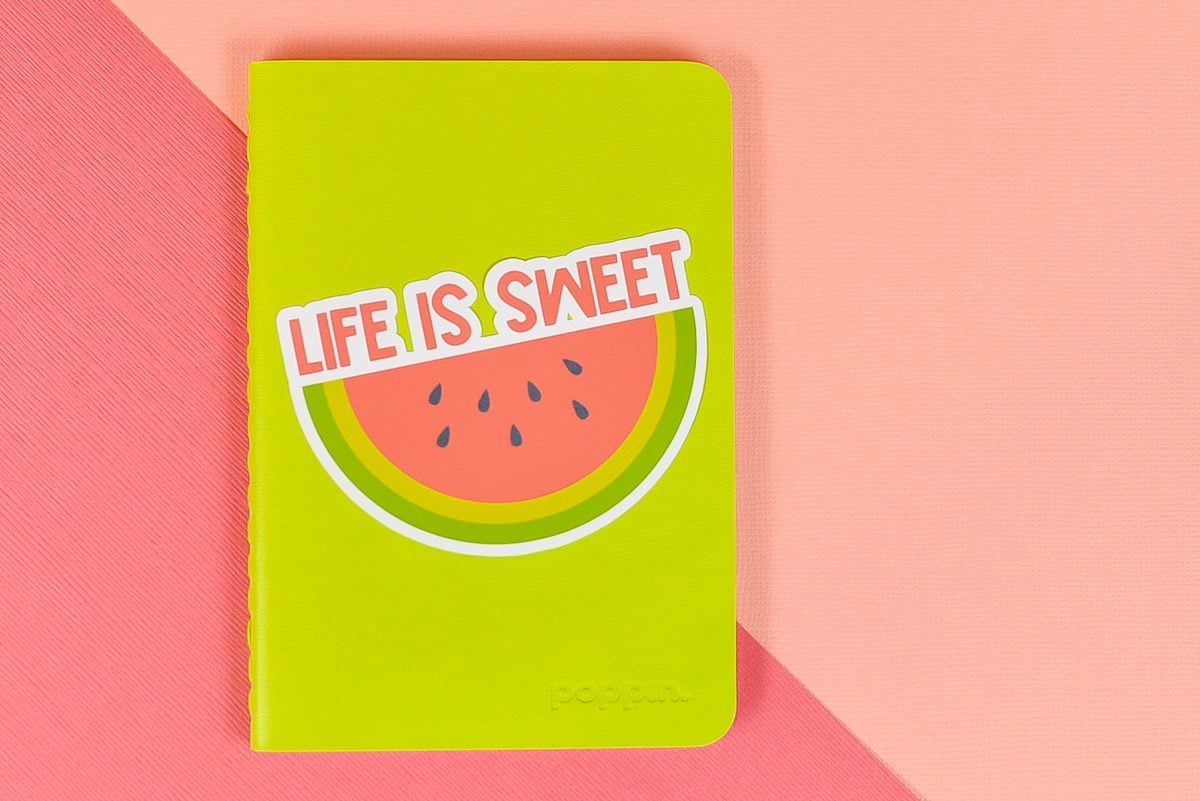 Life is Sweet watermelon sticker on green notebook on pink background