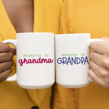 A man and a woman holding coffee cups. One coffee cup is decorated with the words, Promoted to Grandma and the other says Promoted to Grandpa