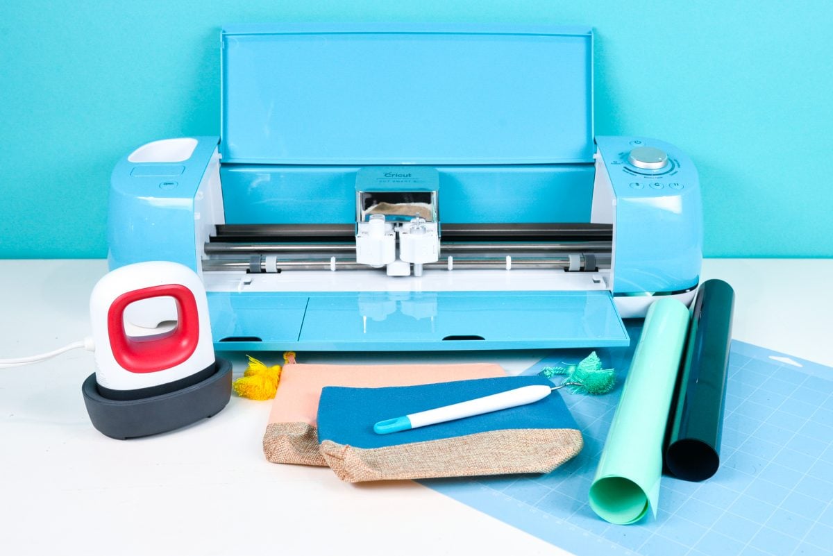 Blue Cricut Explore, EasyPress Mini, blue Cricut cutting mat, black and mint iron on vinyl, two makeup bags, and a weeding tool.