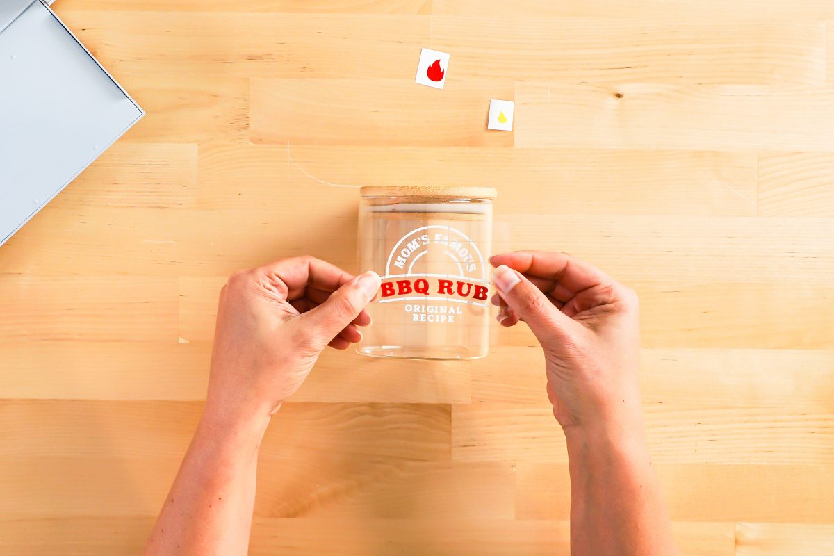 Hands placing transfer tape and decal on jar.