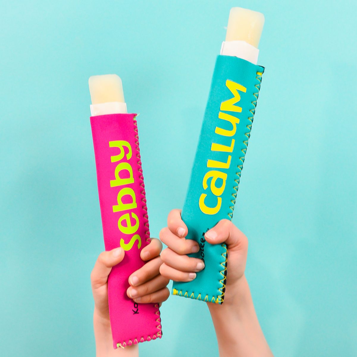 Little kid hands holding two ice pop holders over teal background