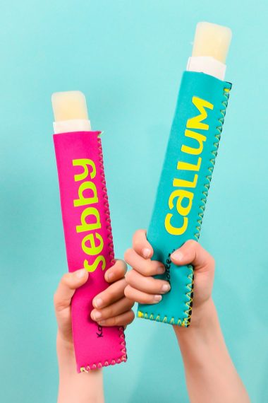 Little kid hands holding two ice pop holders over teal background