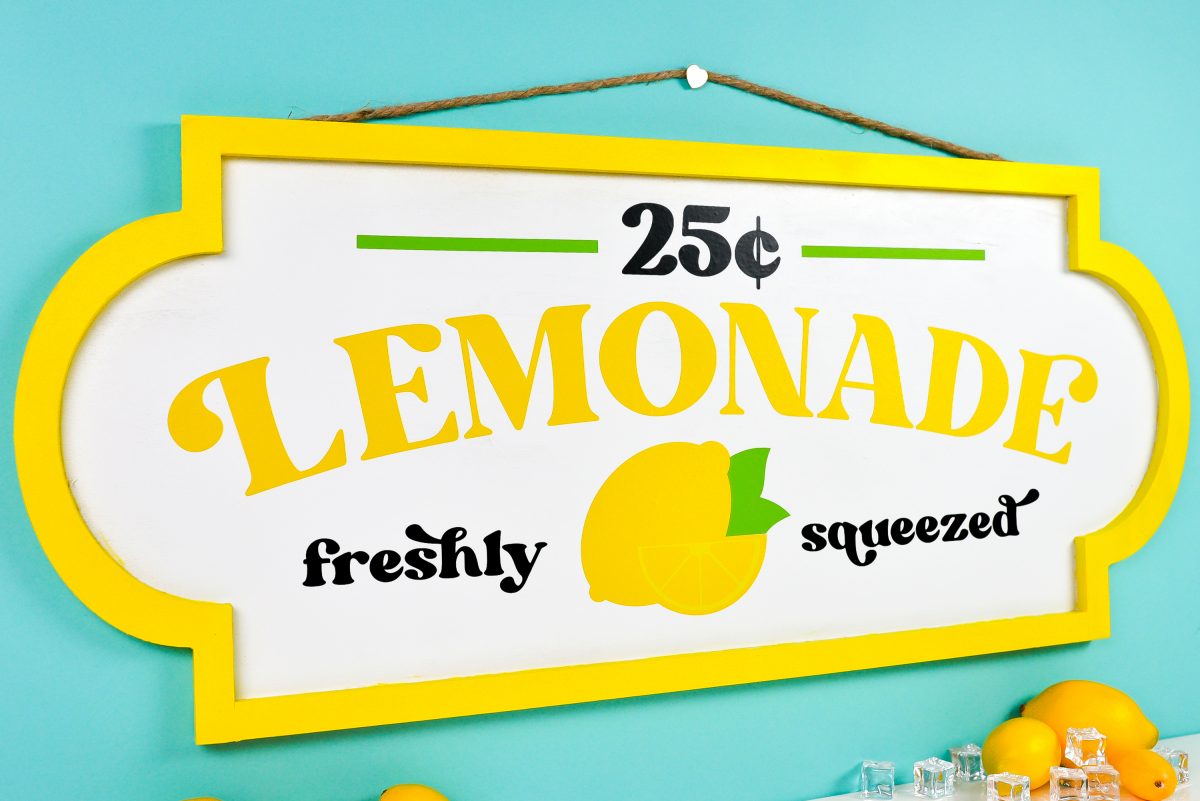 Finished lemonade stand sign on teal background styled with faux lemons and ice