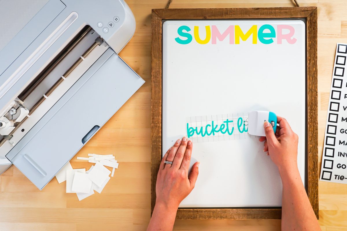 hands using the scraper to burnish the transfer tape to the word "bucket list."