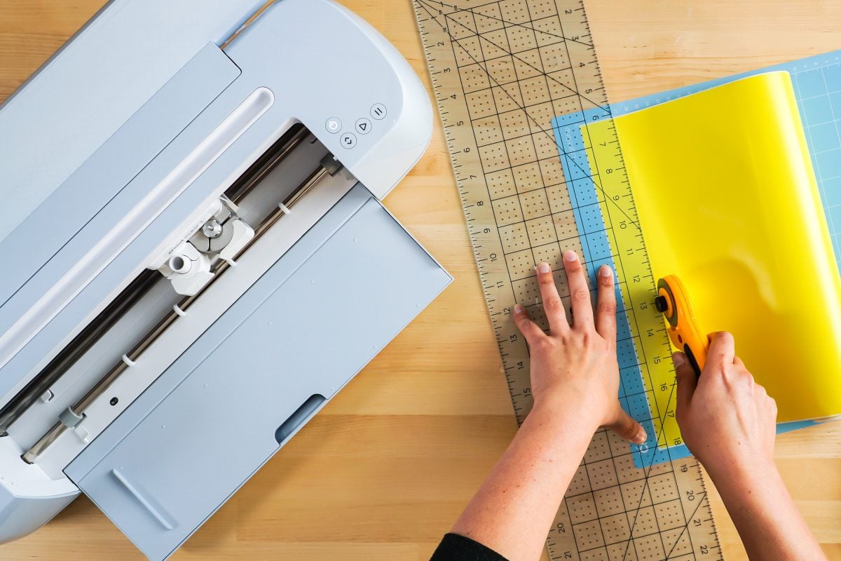 Hands using a ruler and rotary blade to trim down vinyl.