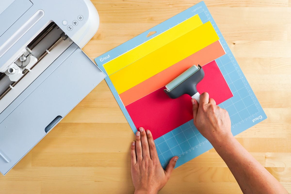 Hands using brayer to smooth vinyl pieces on mat.