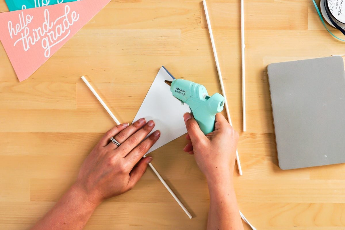 Hands using glue gun to glue pennant to dowel.