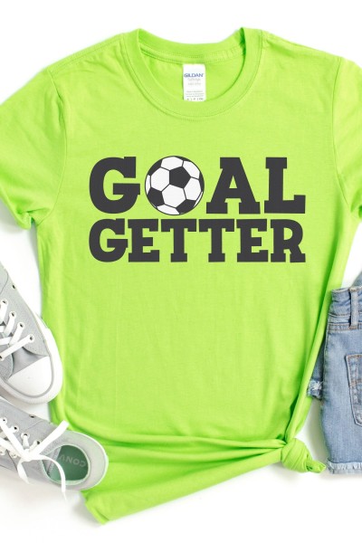 Blue jean shorts with a cell phone in it's pocket, a pair of gray tennis shoes and a bright lime green t-shirt that has a soccer ball on it and the words Goal Getter