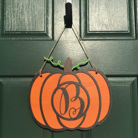 An orange colored wooden pumpkin door hanger personalized with the letter B
