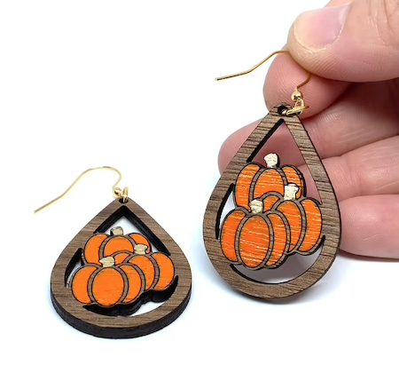 A person holding up one of a pair of wooden pumpkin earrings