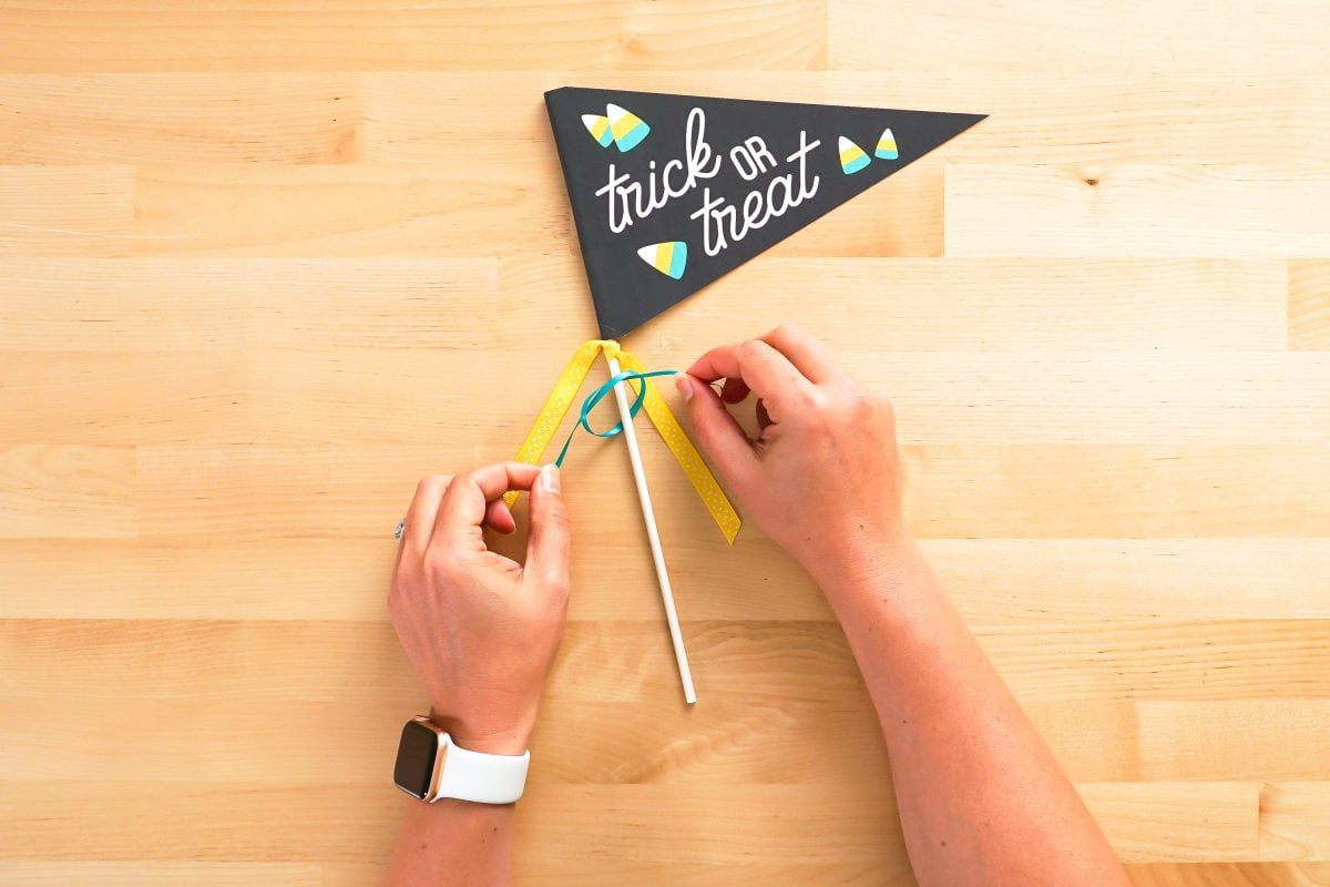 Hands tying ribbon on the dowel below the flag.