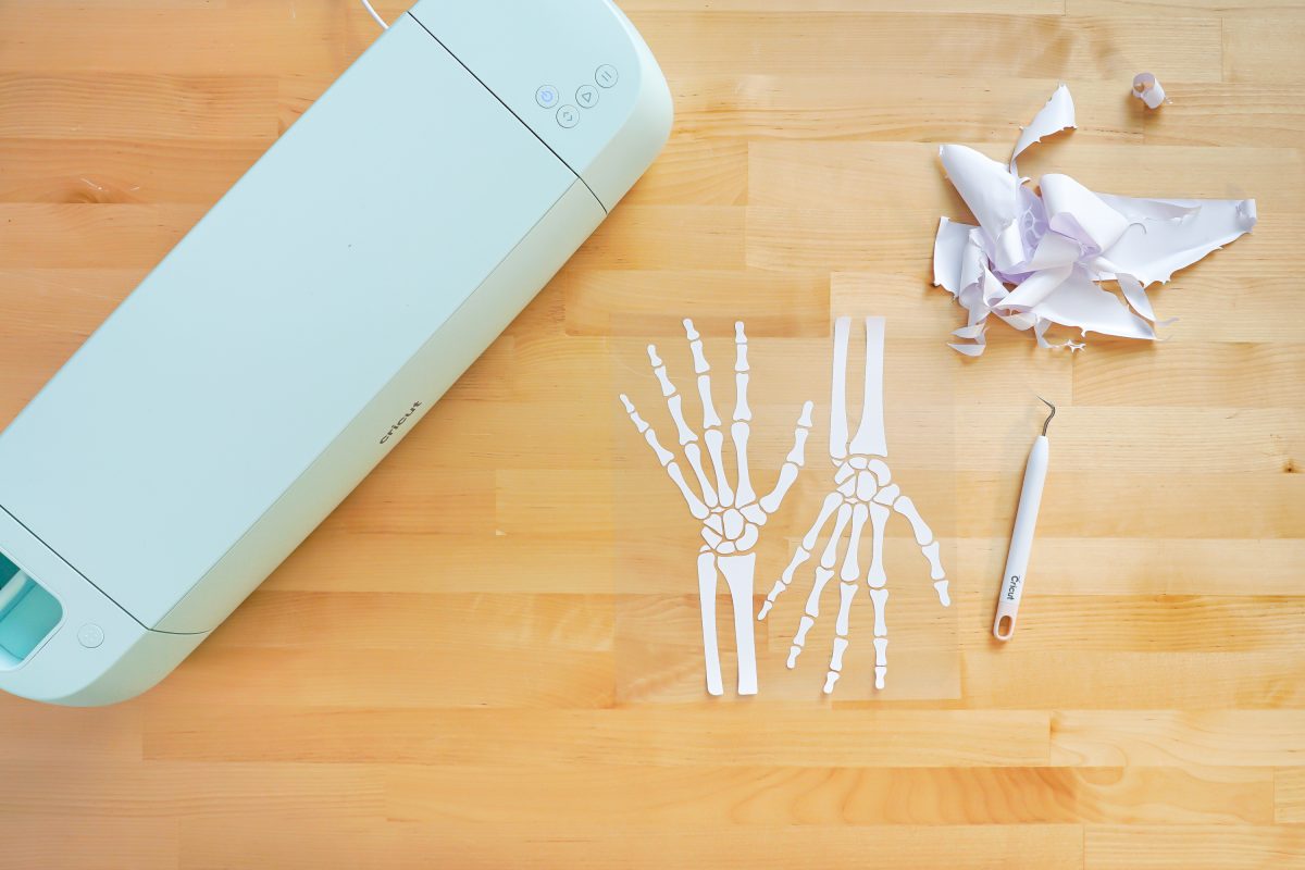 Overhead photo of Cricut Explore 3, and weeded iron on vinyl skeleton hands.