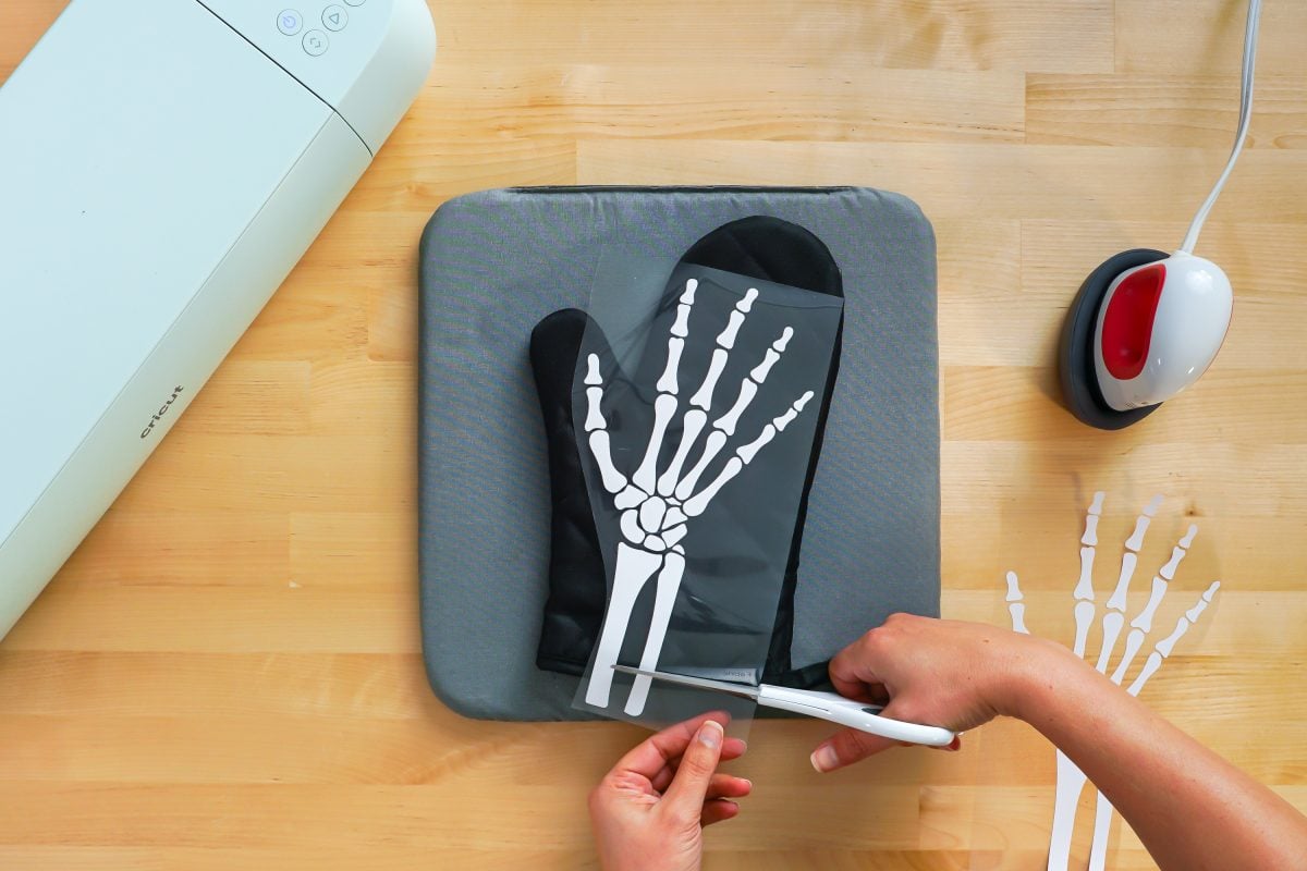 Hands cutting off the bottom of the iron on skeleton hand on black oven mitt.