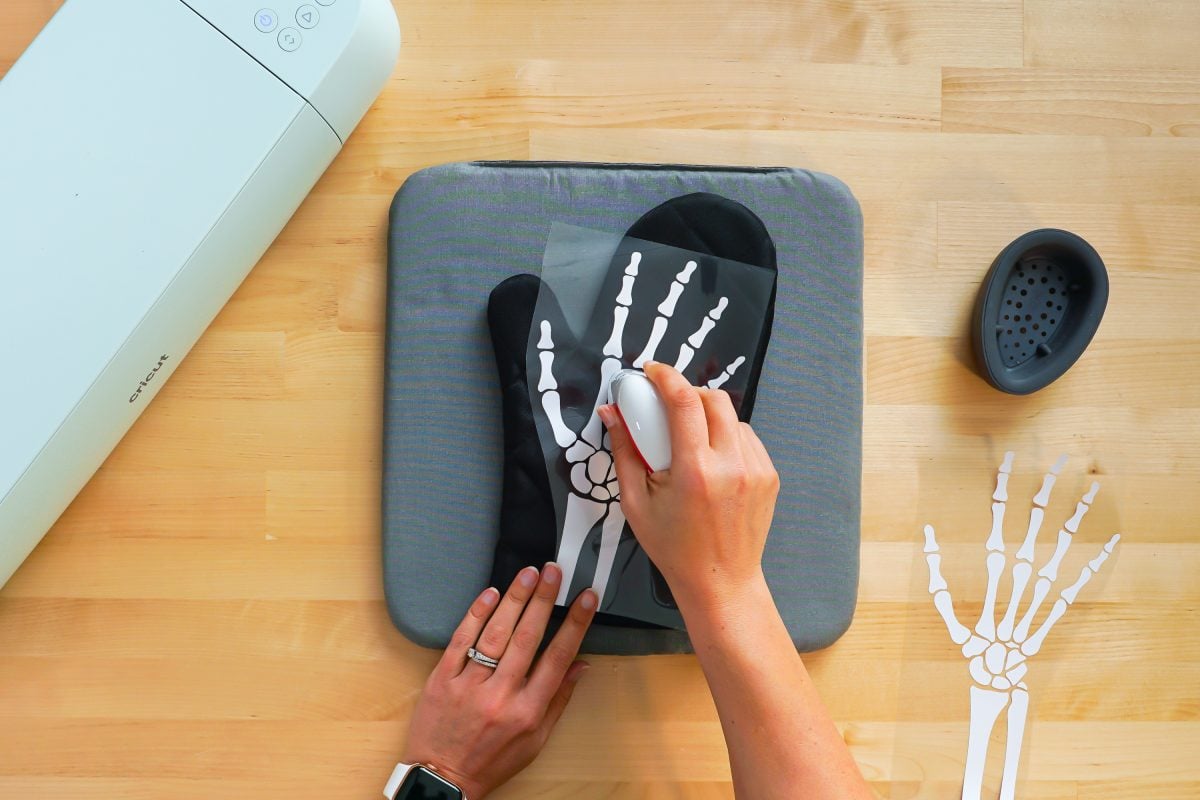 Hands using the EasyPress Mini to adhere the iron on vinyl skeleton hand to the oven mitt.