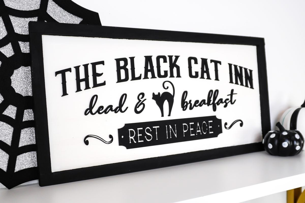 Angle shot of Vintage Halloween Sign: Black Cat Inn sign styled on shelf with Halloween decor