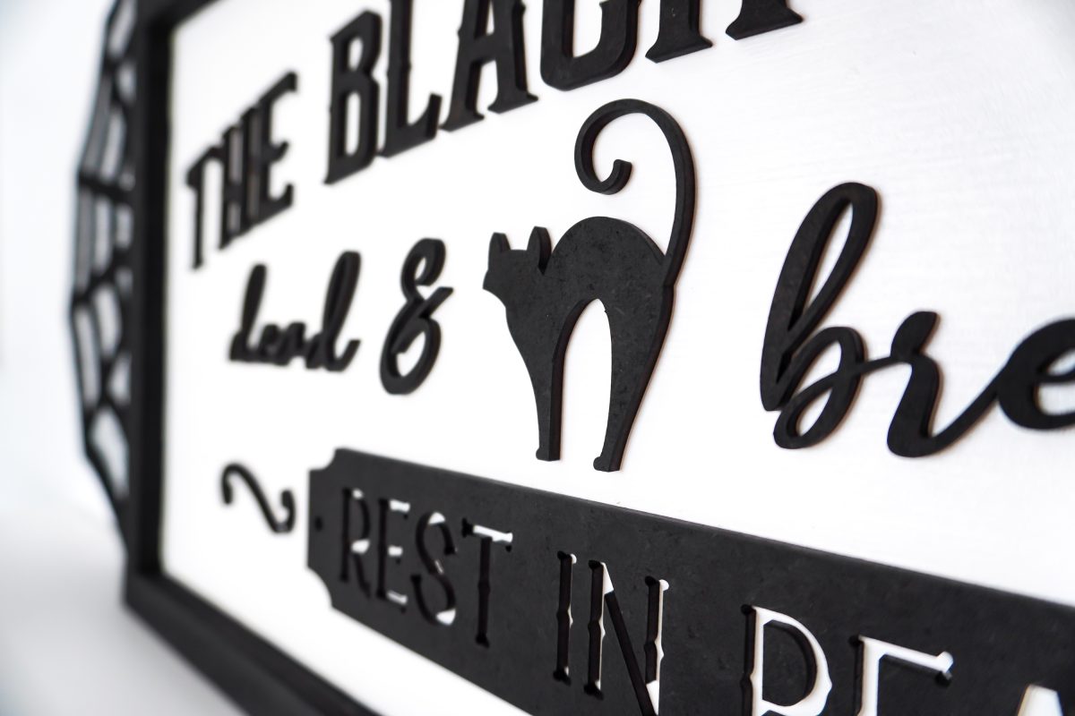 Angle shot of Vintage Halloween Sign: Black Cat Inn sign styled on shelf with Halloween decor