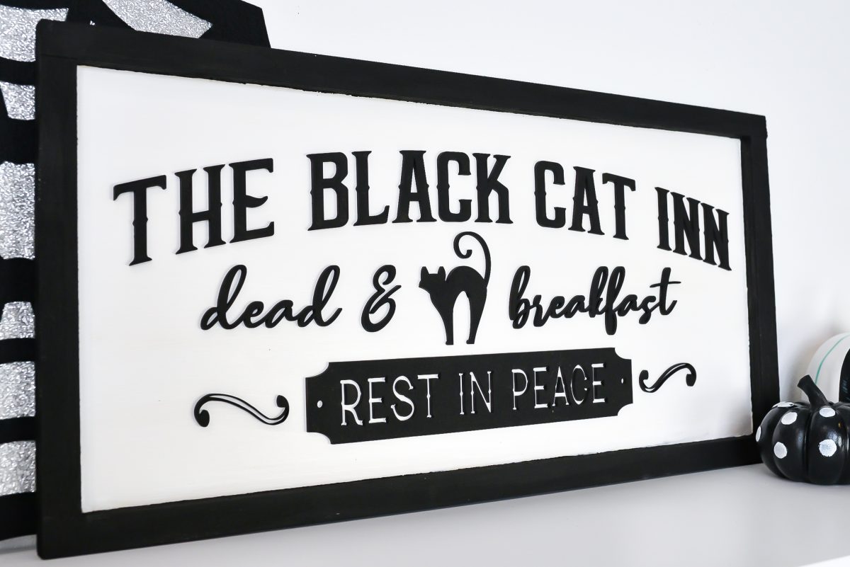 Angle shot of Vintage Halloween Sign: Black Cat Inn sign styled on shelf with Halloween decor