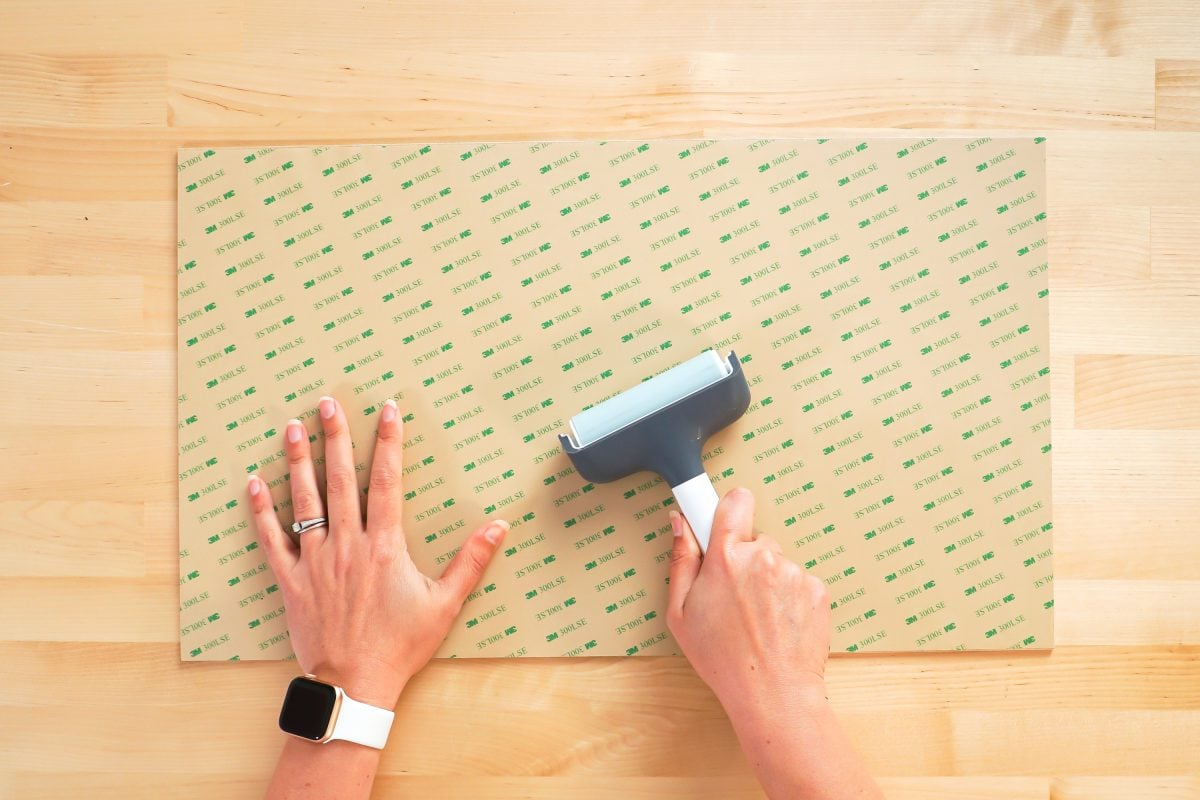 Hands using brayer to adhere 3M adhesive to back of draftboard.