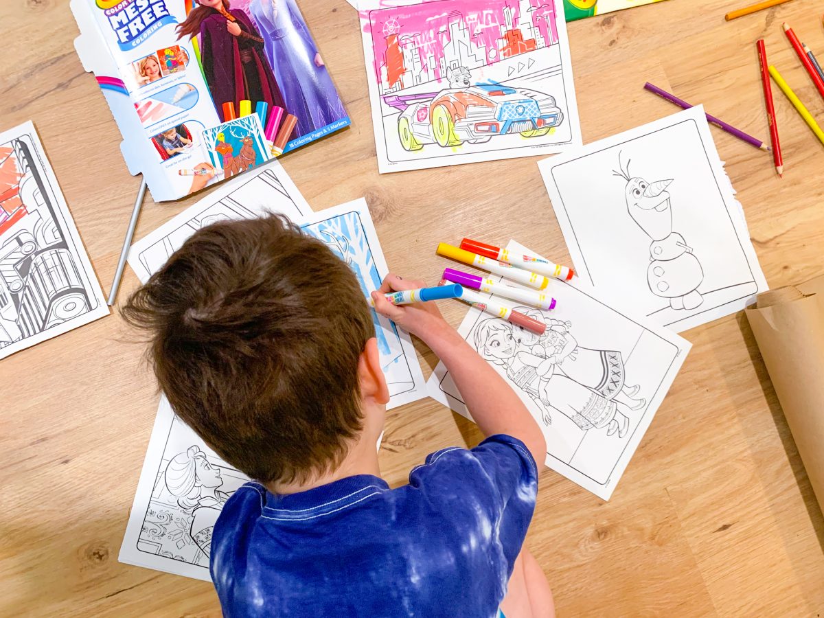 Boy coloring on Crayola Color Wonder sheet surrounded by other coloring sheets and pens.