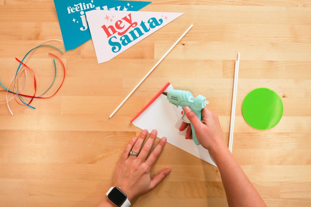 Hand using hot glue gun to attach dowel rod