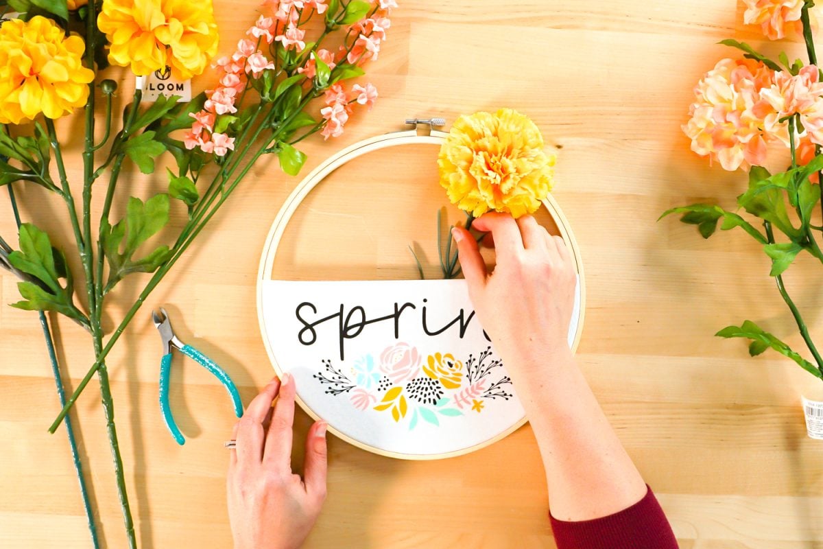Hand adding first floral stem to spring embroidery hoop wreath.