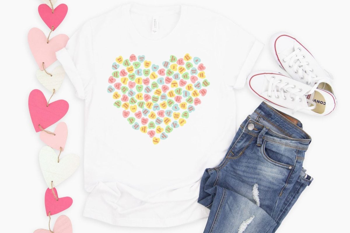 White shirt with sublimated conversation hearts file on it. Staged with jeans, Converse, and a heart banner.