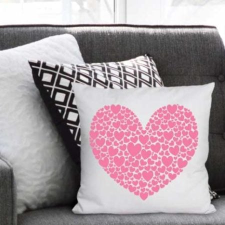 A white throw pillow with a large pink heart made out of small pink hearts