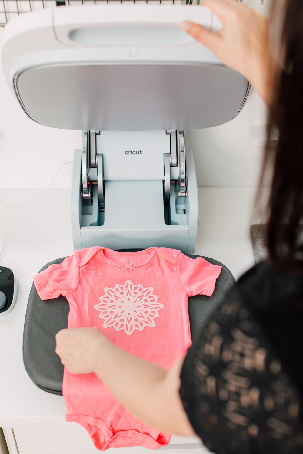 Woman opening Cricut AutoPress to reveal pink onesie inside.