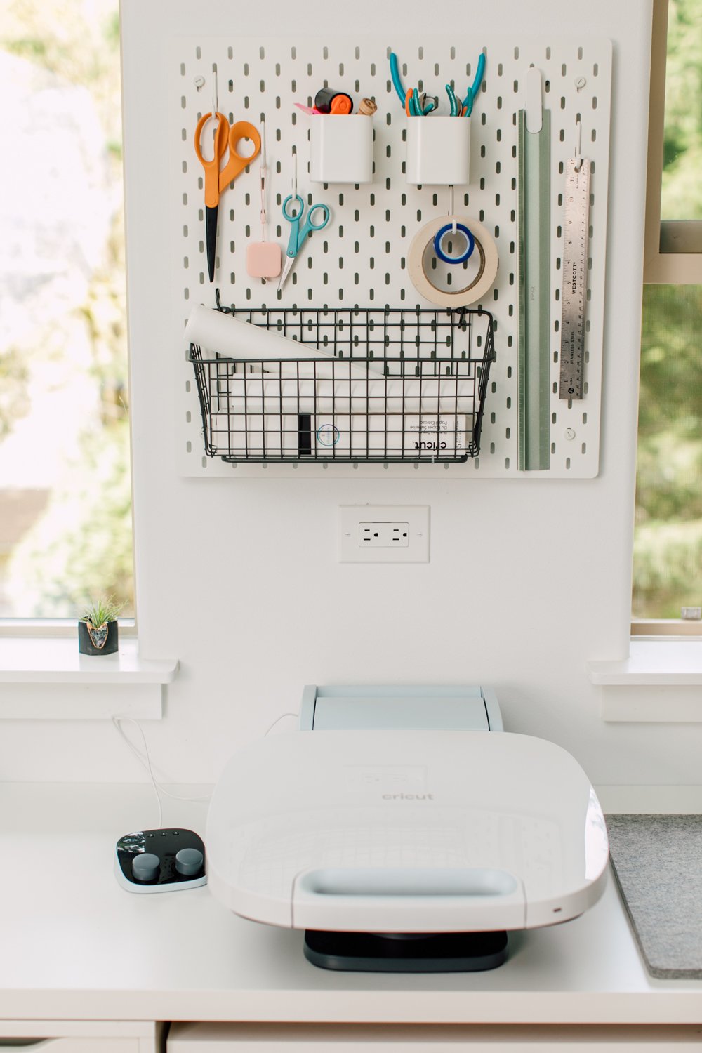 Cricut Maker 3 on desk with pegboard of supplies above.