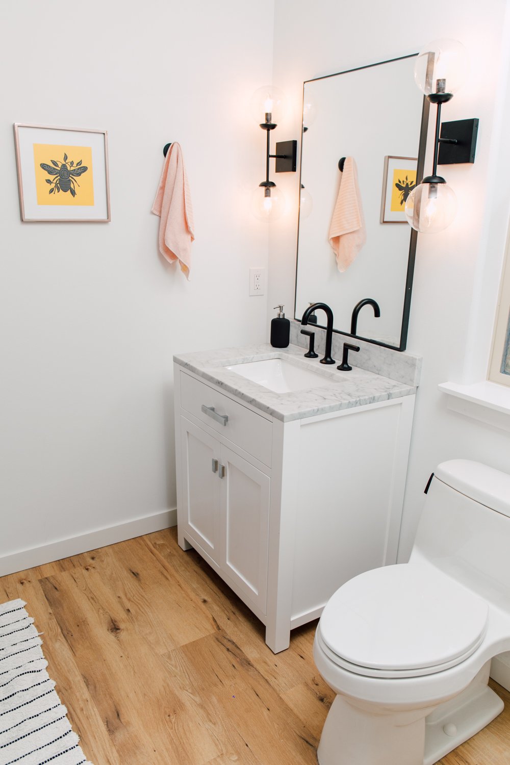 Small bathroom with vanity and mirror, with bee artwork on the wall.