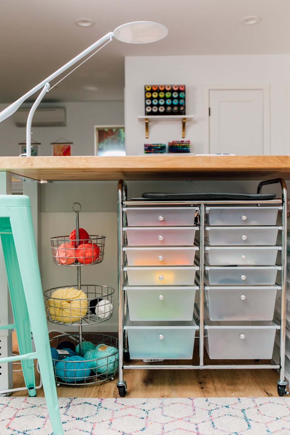 Craft room tour: Worktable with rolling cart of scraps and basket of yarn below. Cricut lamp on top of the desk.