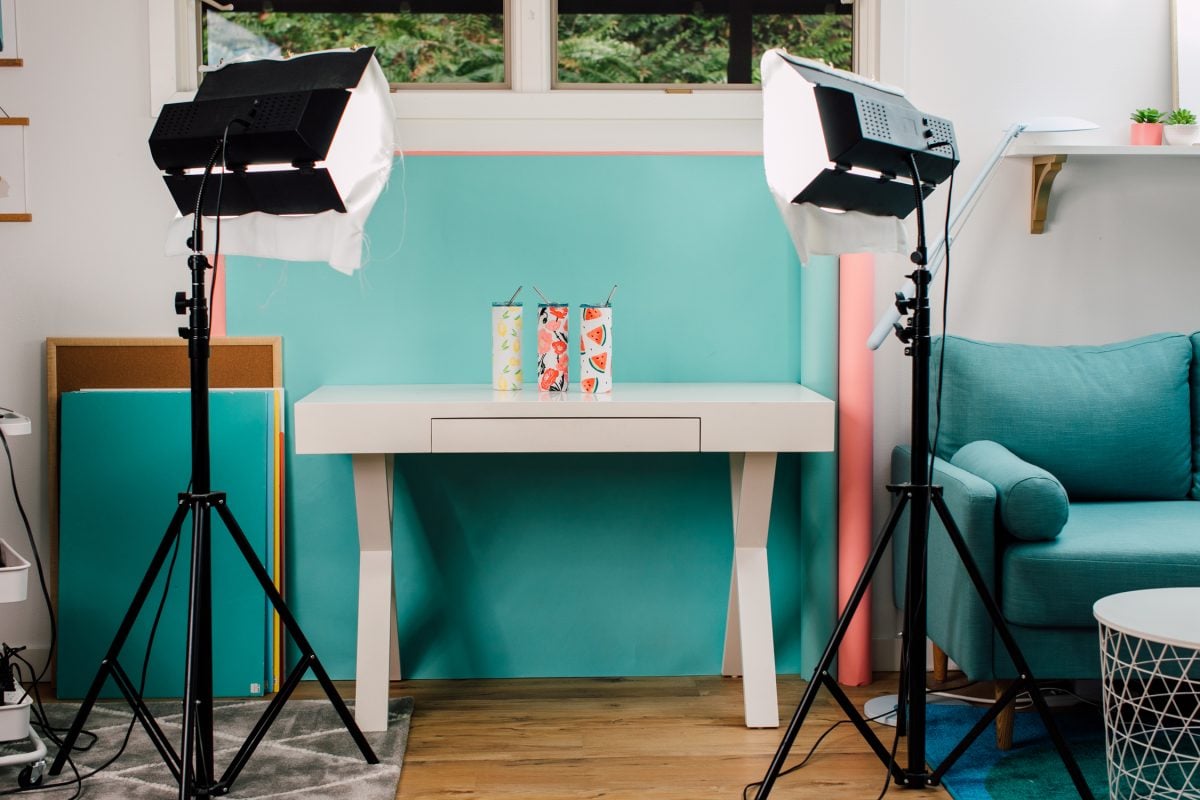 Desk with three tumblers, with blue paper background behind and photography lights shining on them.