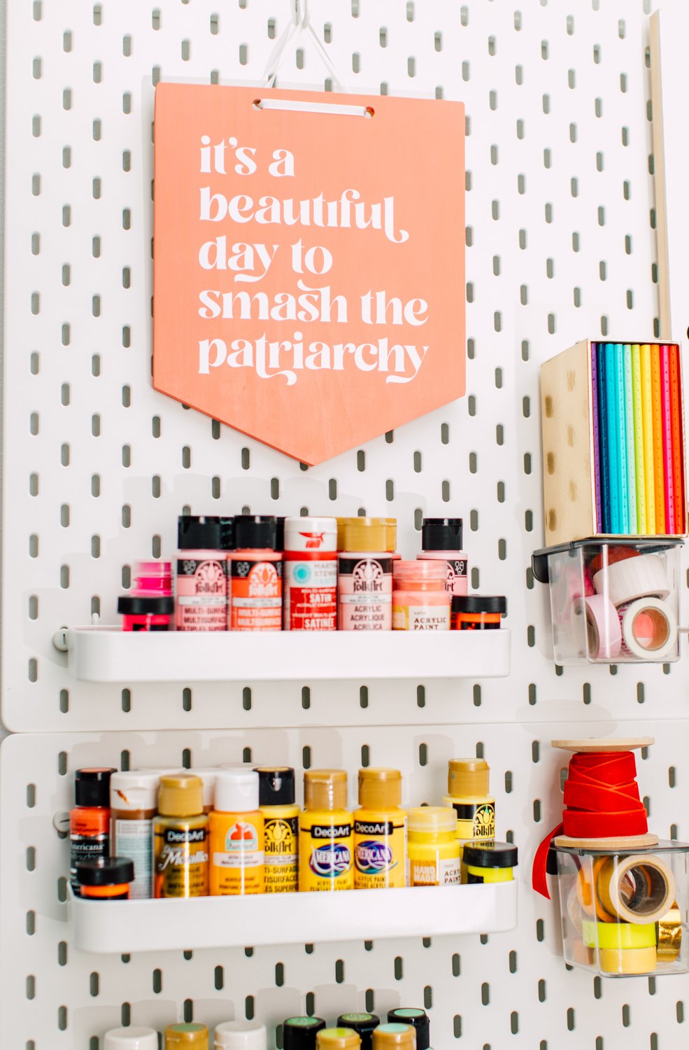 Pegboard with paint and a homemade sign that says "it's a beautiful day to smash the patriarchy"