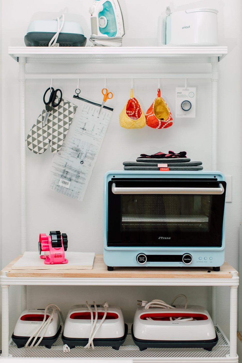 Craft room tour: baker's rack with blue convection oven, several Easypresses, and supplies hanging from hooks.