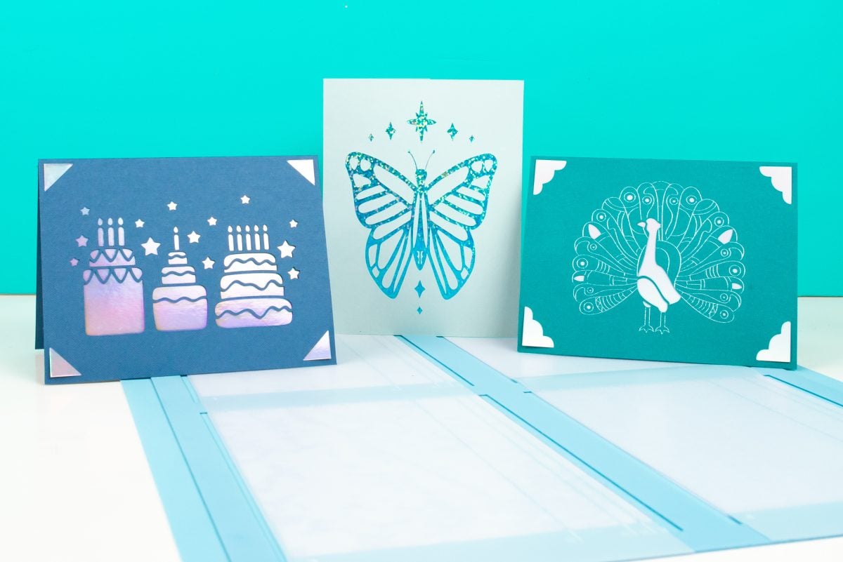 Three Cricut cards and Cricut card mat in front of a teal background. 