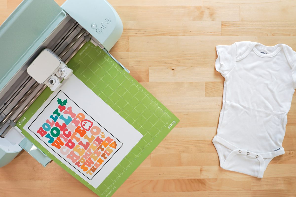 Overhead shot of Cricut with print then cut images and white onesie.