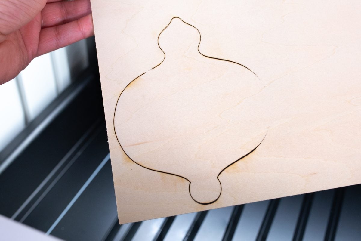 Person holding a piece of basswood with an image of an ornament design that did not cut through the wood