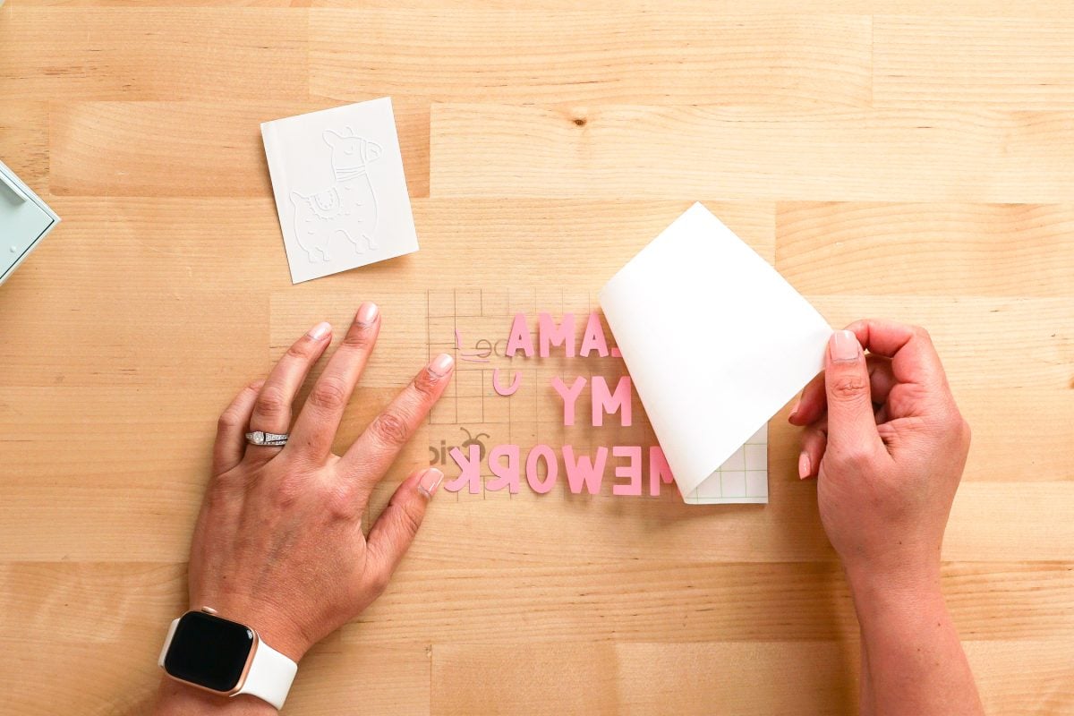 Hands peeling back the backing sheet from a Cricut design