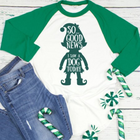 A white and green baseball style shirt with an elf on it and the saying, So, the good news, I saw a dog today
