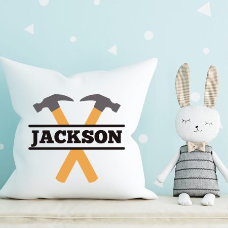 A cute stuffed bunny sitting next to a white pillow that has a hammer monogram on it
