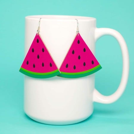 A pair of watermelon earrings hanging on the side of a white coffee mug